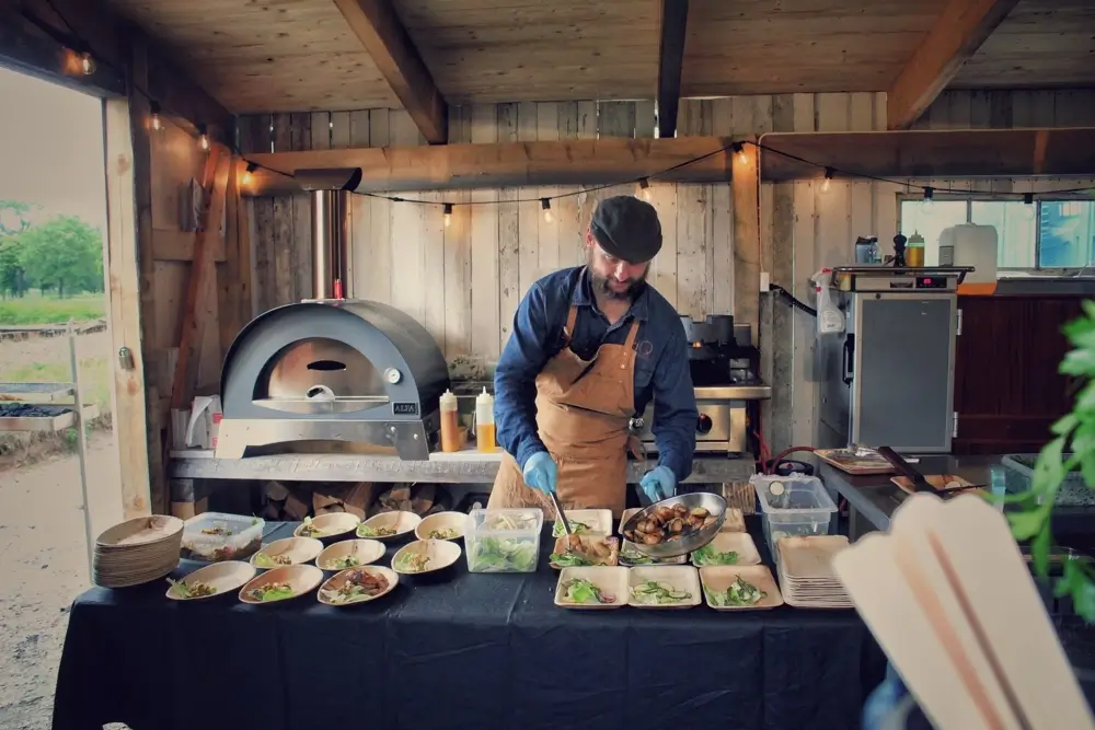 A Chef in an outdoor kitchen placing wok vegetables on wooden plates